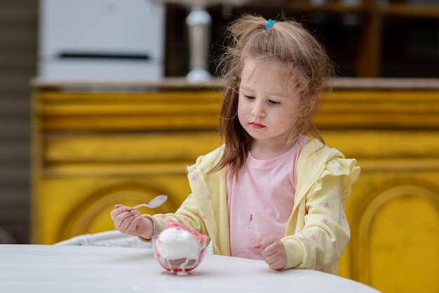 女の子がおもちゃの貯金箱を持ってテーブルに座っています。