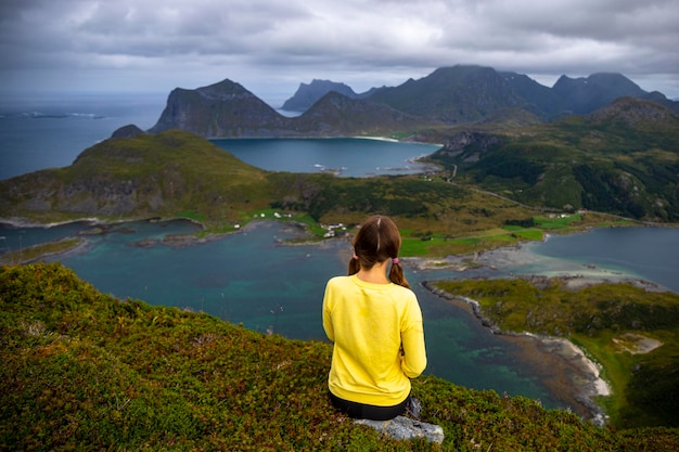 Girl sits on top of Offersoykammen enjoying the panorama of the lofoten islands, Norway hiking