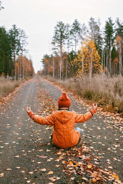 Photo girl sits in yoga pose on road in fall forest deep in thoughts daydreaming mental health autumn