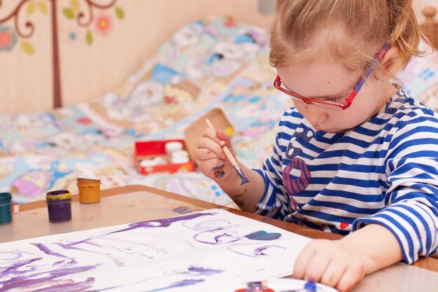 Фото Девушка сидит за столом и рисует краски на белой бумаге