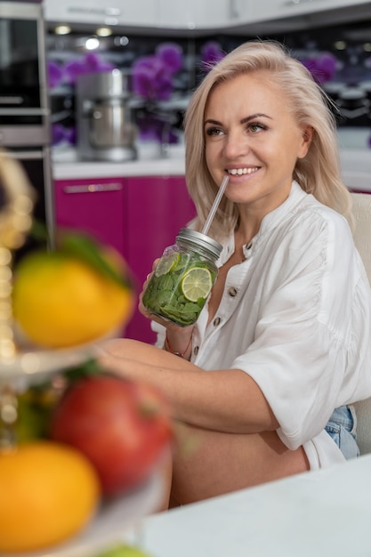 Foto ragazza seduta sullo sfondo di un vaso di frutta che tiene la limonata nelle sue mani