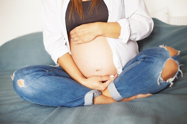 Girl sitting on bed in bedroom and hugging her pregnant belly with hands Concept of maternal health