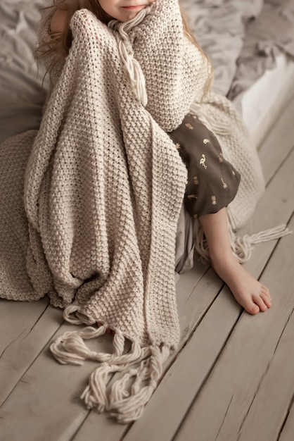 Girl sitting on the bed in the bedroom wrapped in a blank