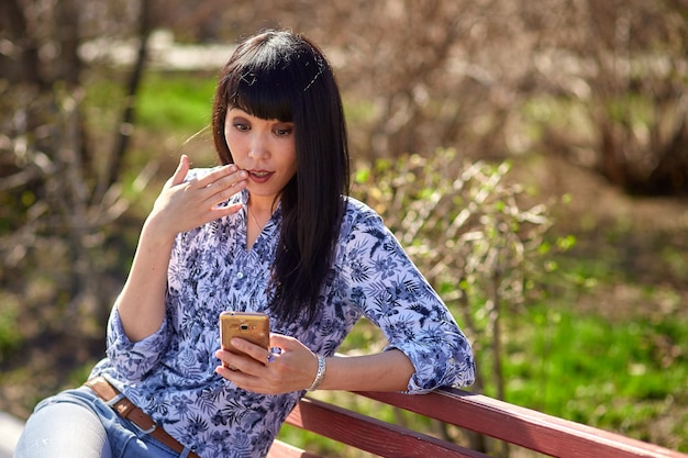 девушка сидит на скамейке в парке с телефоном в руке