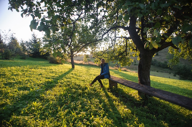 Girl sitting on a bench under the trees in the mountains