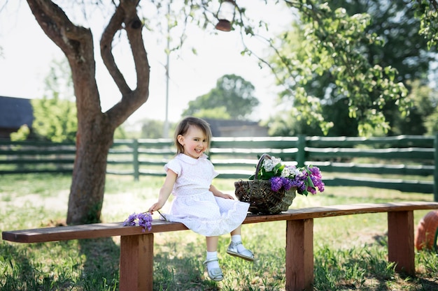 Girl sitting on a bench in the village with a basket of lilacs