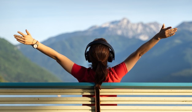 Girl sitting on a bench with her arms up with stalk hat on and red dress relaxing looking at the mountains by a lake