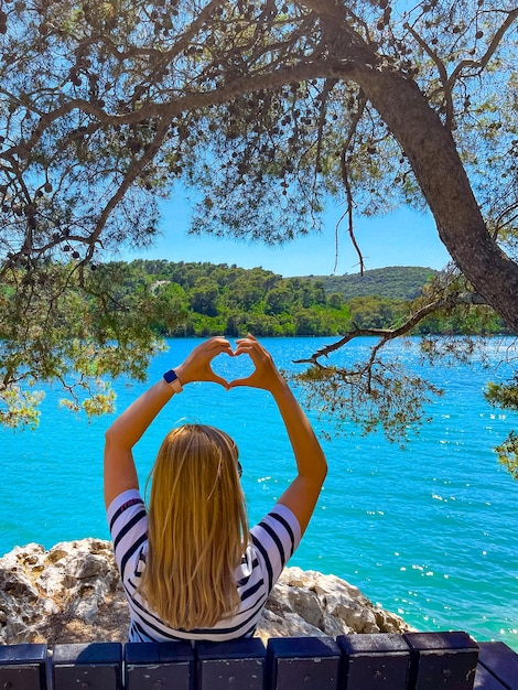 Foto una ragazza seduta su una panchina con la schiena sulla riva del parco nazionale di mljet in croazia, foto verticale