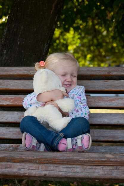 Girl sitting  on a bench with teddy at the park.