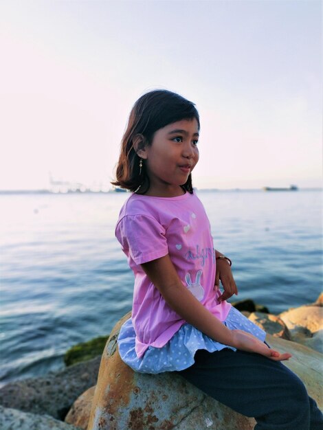 Photo girl sitting by pink sea against sky