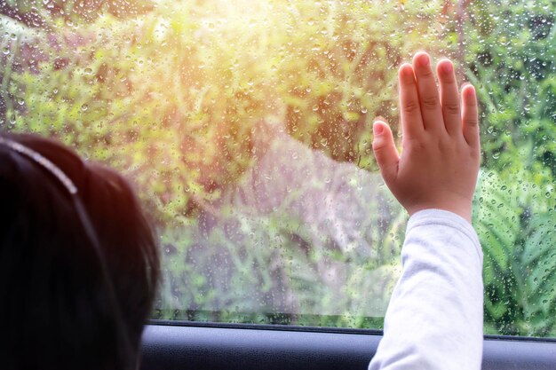 車の中に座っている女の子車のガラスに手を当てる降る雨を見る季節が起こる自然の状態について学ぶ