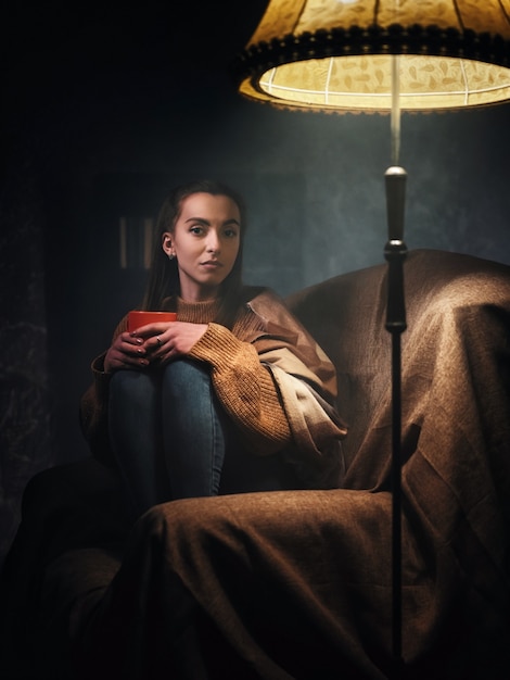 Girl sitting on a chair at night in the light of the lamp