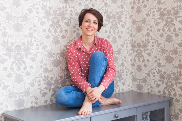 Girl sitting on chest of drawers at home.