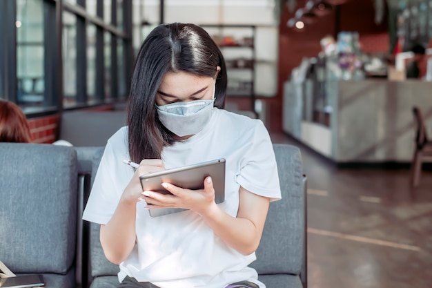 A girl sitting at a coffee shop By including the mask To prevent the corona virus