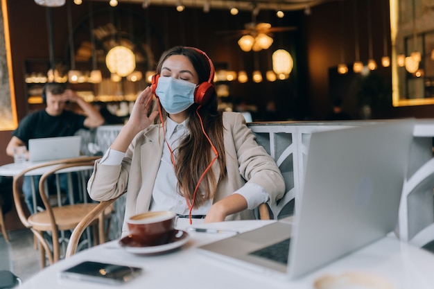 Una ragazza seduta in una caffetteria con le cuffie focolaio di coronavirus