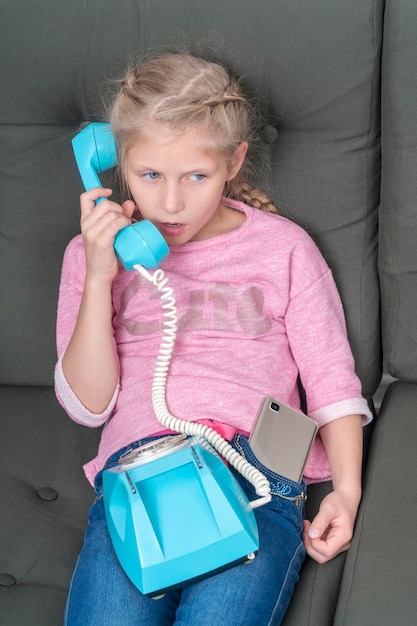 Photo girl sitting on the couch is talking on the old phone, although a new smartphone sticks out of her pocket