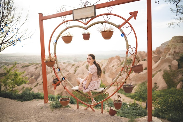 Girl sitting on a decorated heartshaped bench on a viewpoint and admiring view of Cappadocia