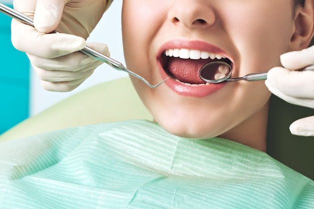 Девушка сидя на зубоврачебном кресле с открытым ртом во время устного осмотра вверх пока доктор. Посещение стоматологического кабинета. Концепция стоматологии.