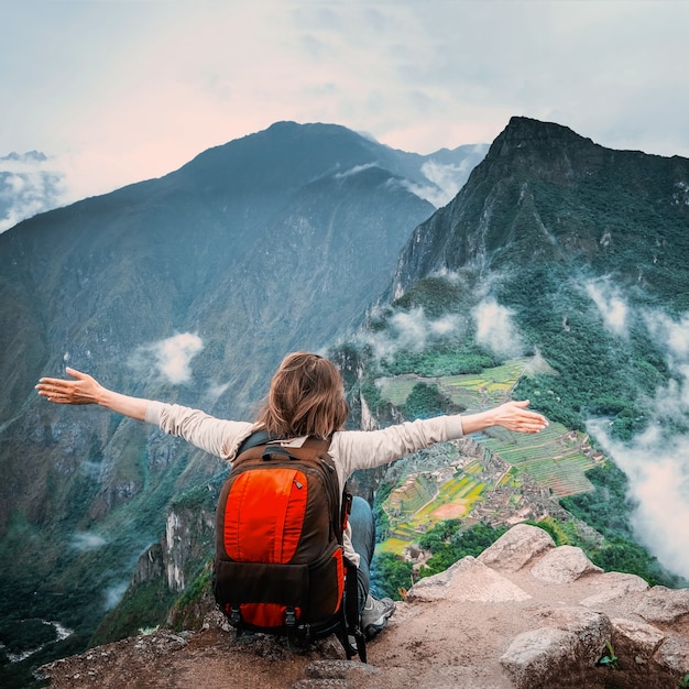 Foto ragazza seduta sul bordo della roccia e godersi il paesaggio di machu picchu