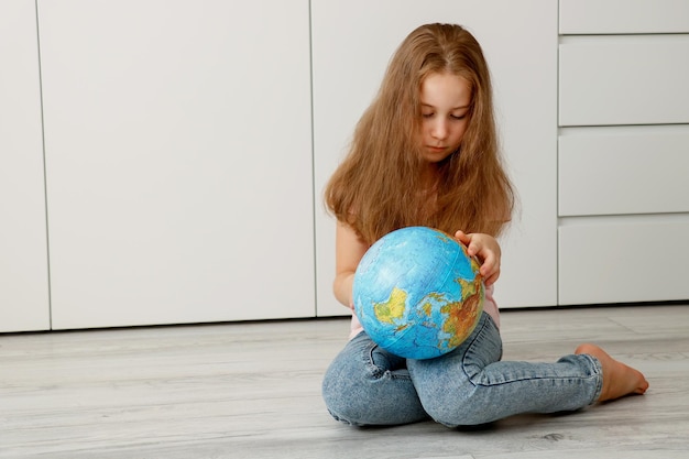Девушка, сидящая на полу, внимательно рассматривает глобус в руках