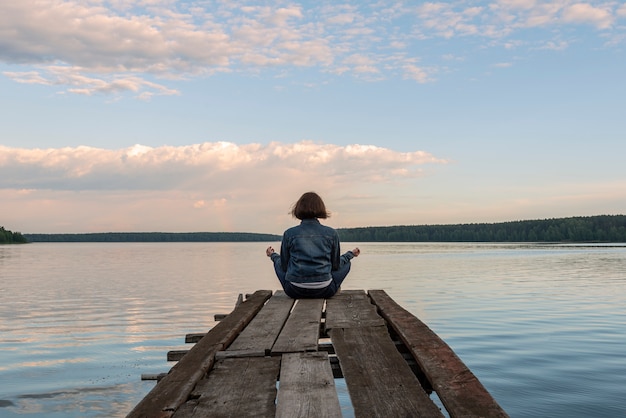 Girl sitting in lotus position on a wooden pier