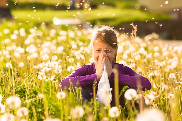 Девушка сидит на лугу с одуванчиками и имеет сенную лихорадку или аллергию