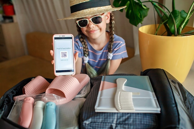 Girl sitting near suitcase packed for vacation and demonstrates the vaccination proof message