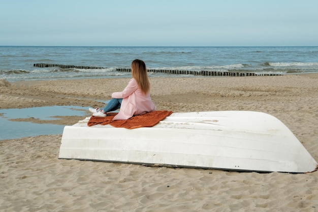 Photo girl sitting on an overturned boatyoung woman sitting on old overturned boat outdoors sea