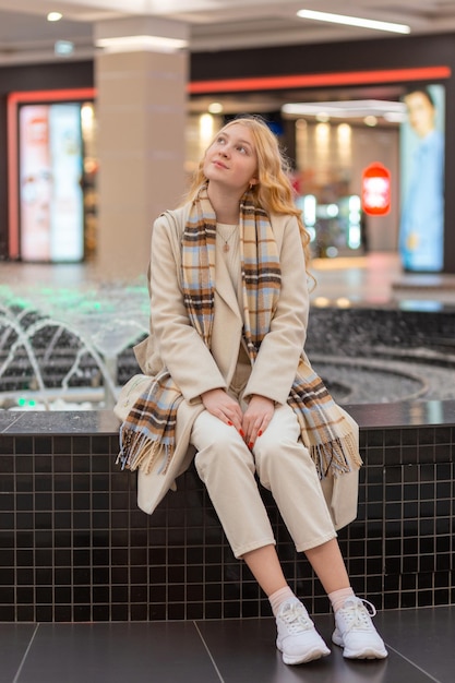 Girl sitting on the parapet at the mall near the fountain