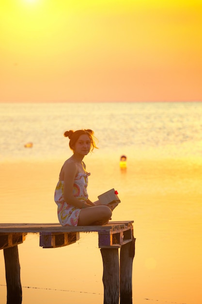 Girl sitting on a pier and reading at the sunset time