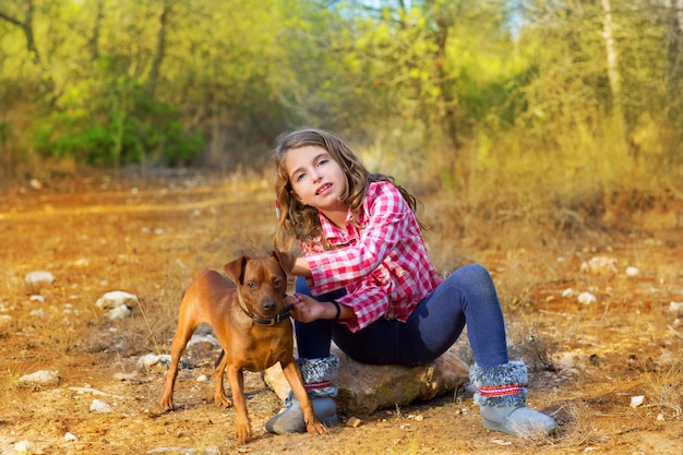 girl sitting in the pine forest holding little dog