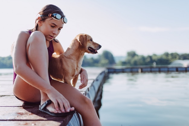 Girl sitting on the river dock with her dog