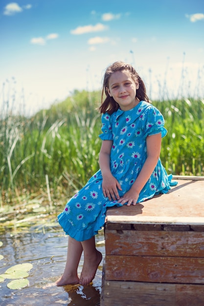 Girl sitting on river pier and wetting her bare feet in water