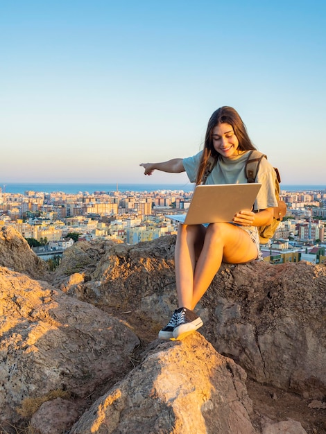 Girl sitting on a rock on a hill showing the landscape with her
laptop digital nomad traveling