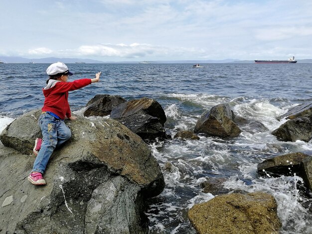 Foto ragazza seduta su una roccia sulla riva contro il cielo