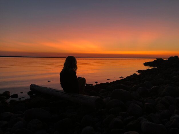 Foto ragazza seduta sulle rocce sulla spiaggia durante il tramonto