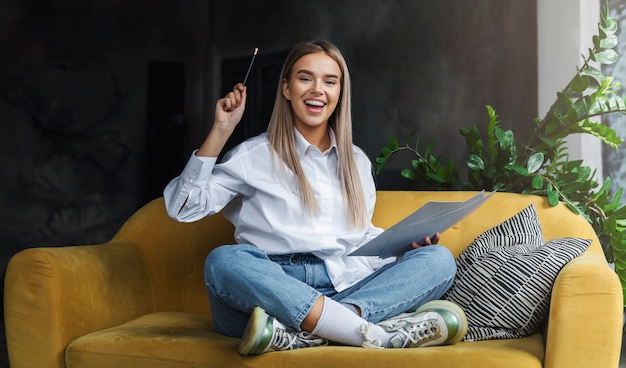 Girl sitting on sofa, drawing on paper with pencil.