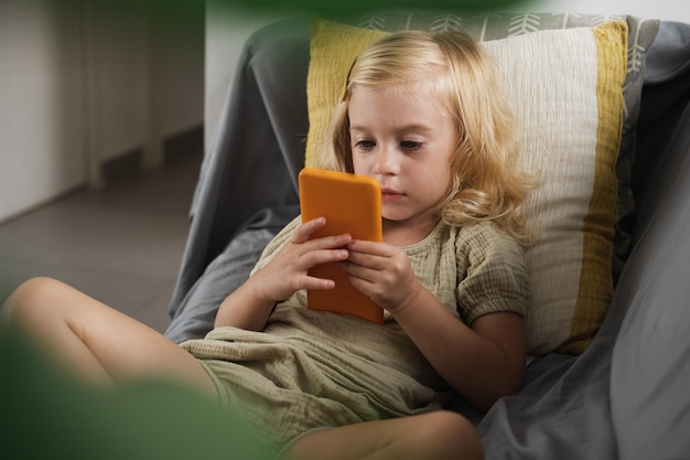 Girl sitting on sofa looking at smartphone at home kid playing gamewatching cartoons