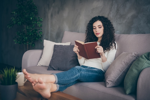 ソファに座って本を読んでいる女の子モダンなロフトインダストリアルスタイルのインテリアリビングルームの屋内で長い交差した脚