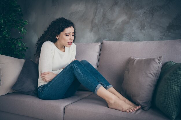 girl sitting on sofa suffering from indigestion cause in modern loft industrial style interior living-room indoors