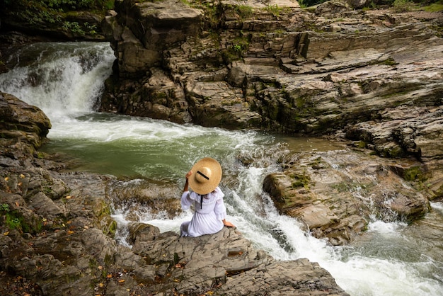 A girl sitting on the stone among the mountains and looking at the river.