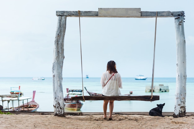 Девушка сидит на качелях на тропическом пляже