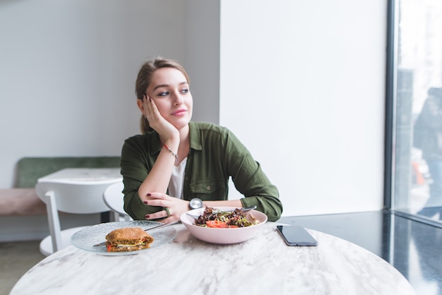 Girl sitting at table in restaurant and looks in window.