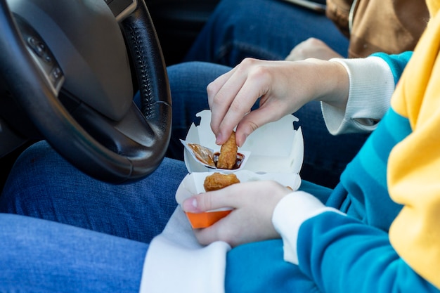 車のハンドルに座ってナゲットをソースに浸して食べる女の子ファーストフードの持ち帰り用スナック