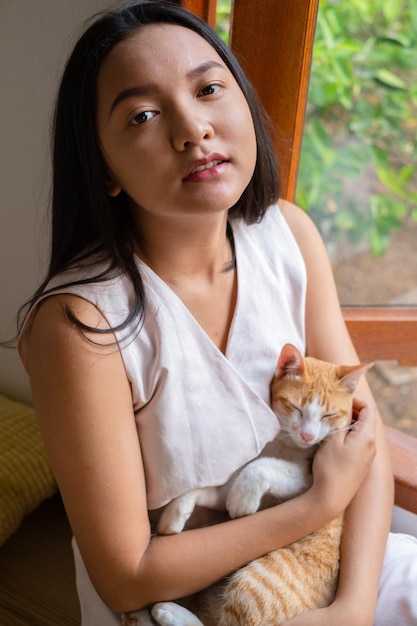 The girl sitting with a cat at the window at home