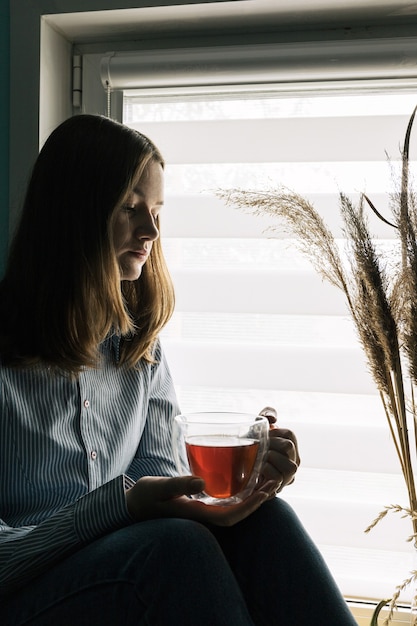 Girl sitting with a pensive expression on her face holding a cup of teaCopy space