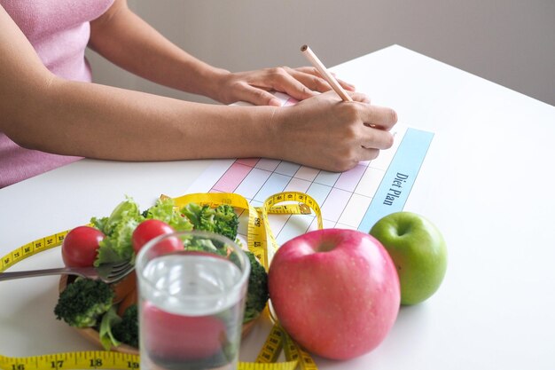 A girl sitting and writing a diet plan weight loss concept eat food that is  good for the body Such as fruits and vegetables | Premium Photo