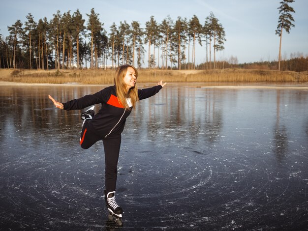 Girl skates on the ice of a forest lake raises her leg