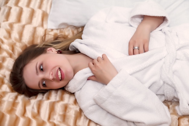 Girl of Slavic appearance in white coat on bed in hotel room