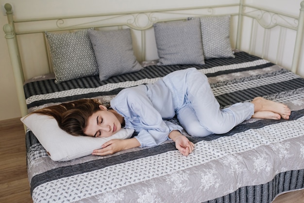 The girl sleeping in her pajamas on the bed in her room. Stylish gray-white interior.